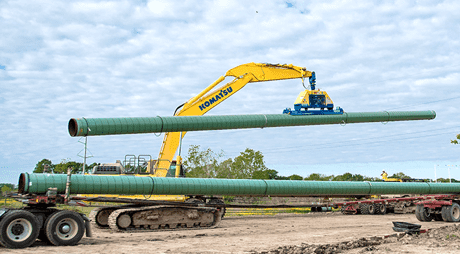 A large crane moves a piece of pipeline over a construction zone